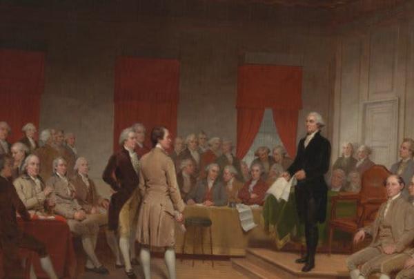 On a dais in the center, George Washington, holding pages of a document in his hands and wearing a dark suit, addresses the assembly. Most of the mean are seated at tables arrayed around the room. This painting depicts a roomful of white men in wigs and 18th-century dress.