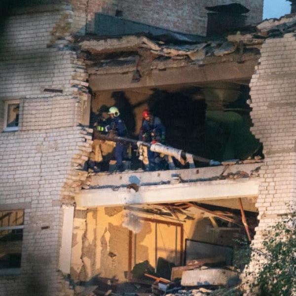 Ukrainian rescue workers clear debris from a destroyed floor of a military educational institution with part of its exterior wall missing.