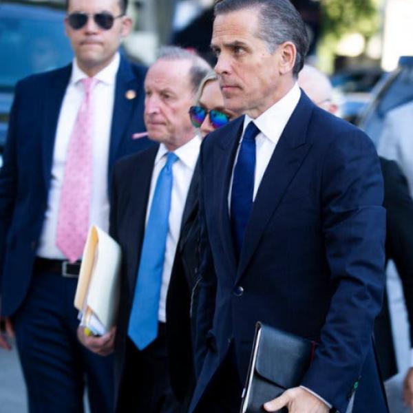 Hunter Biden in a blue suit and tie is surrounded by other people in suits.