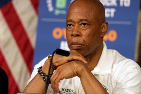 Mayor Eric Adams sits before a microphone, his hands stacked in front of him.