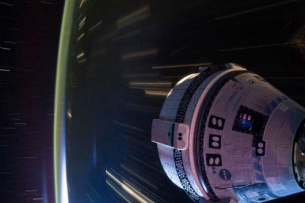 The Boeing Starliner spacecraft over a darkened Earth with blurred lights.