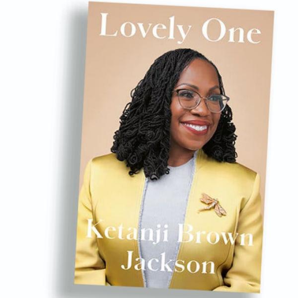 She is smiling and looking off to the right. The cover of “Lovely One” is a photograph of Ketanji Brown Jackson wearing a yellow jacket over a gray shirt, with a large gold dragonfly brooch on her chest.