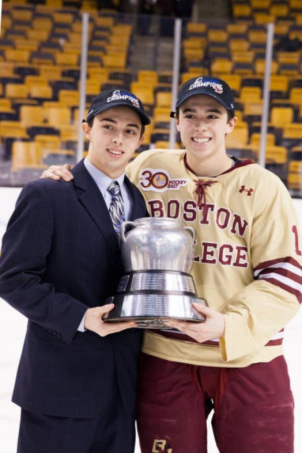 They are holding a trophy. John has one arm around Matt. Matthew Gaudreau, who is wearing a suit, stands with his brother, John, who is wearing a Boston College jersey.