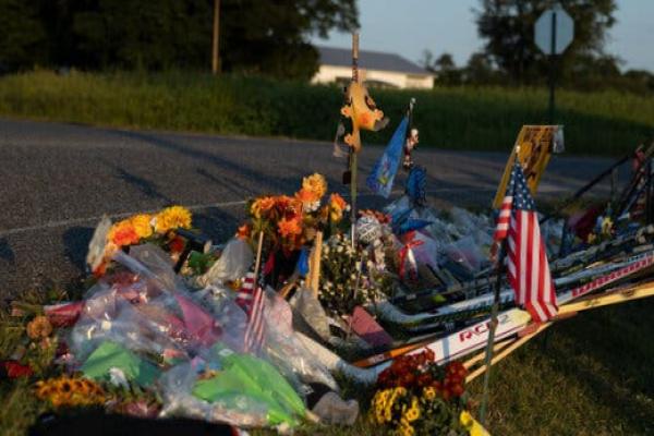 Hockey sticks and flowers form a makeshift memorial at the side of a road.