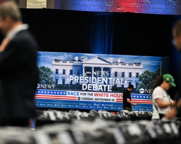 People out of focus stand in the foreground of a room with a large sign that reads 