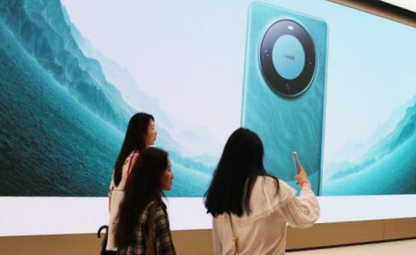 Three people standing in front of a large promotional image of the Mate 60 phone at the Huawei store in Shanghai.