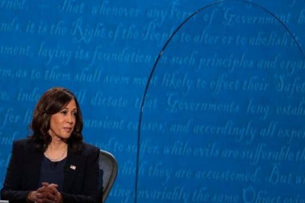 Kamala Harris sitting at a table, behind a sheet of plexiglass, during her debate against Mike Pence in 2020.