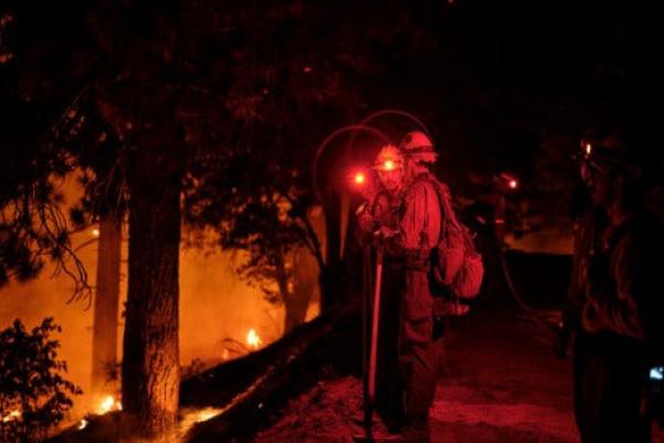 People wearing hard hats and red headlamps stand on top of a ridge of trees with small scattered fires burning.