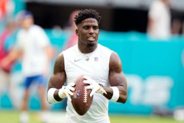 Tyreek Hill, wearing a white tank top and holding a football, looks off.