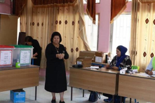 A woman in a black dress standing at a polling station.