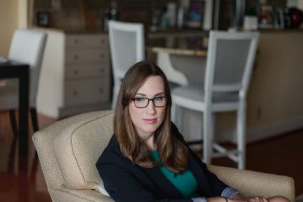 Sarah McBride, wearing glasses, is seated in a tan chair.