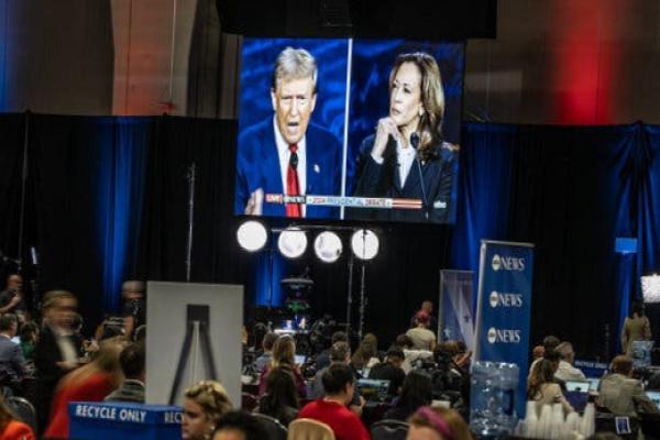 Reporters in the “spin room” at the debate, with a large screen in the background showing Donald Trump and Kamala Harris.