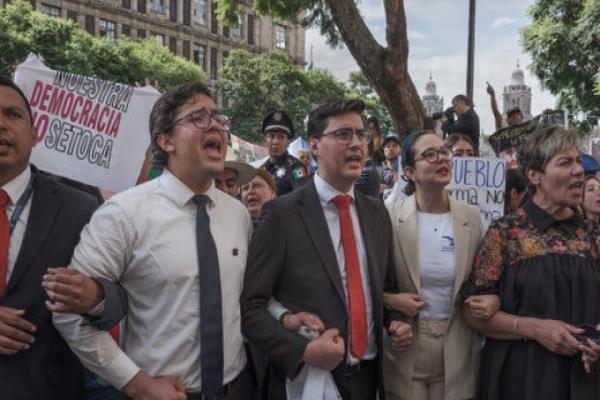 Protesters wearing business attire lock arms and shout chants outside of a court building.